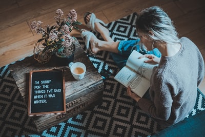 女人坐在咖啡桌附近的地毯在阅读书
